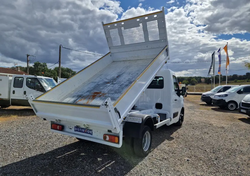 Renault Master Benne blanc vu 3/4 arrière avec benne relevée et roues jumelées sur terrain extérieur.