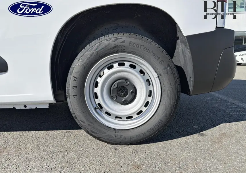 Gros plan sur la roue arrière droite d’un utilitaire blanc avec jante acier et logo Ford visible.