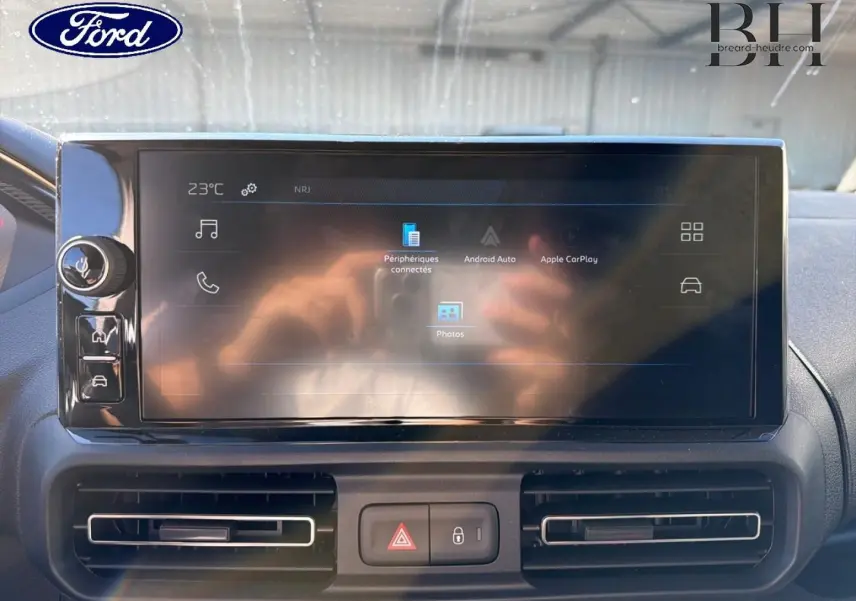 Écran tactile central du tableau de bord d’un Peugeot Partner blanc, avec commandes et aérateurs visibles.