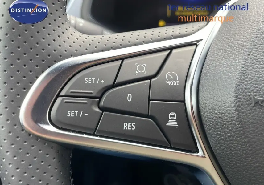 Gros plan sur les commandes de régulateur de vitesse au volant perforé du Renault Captur E-Tech hybride rouge toit noir.