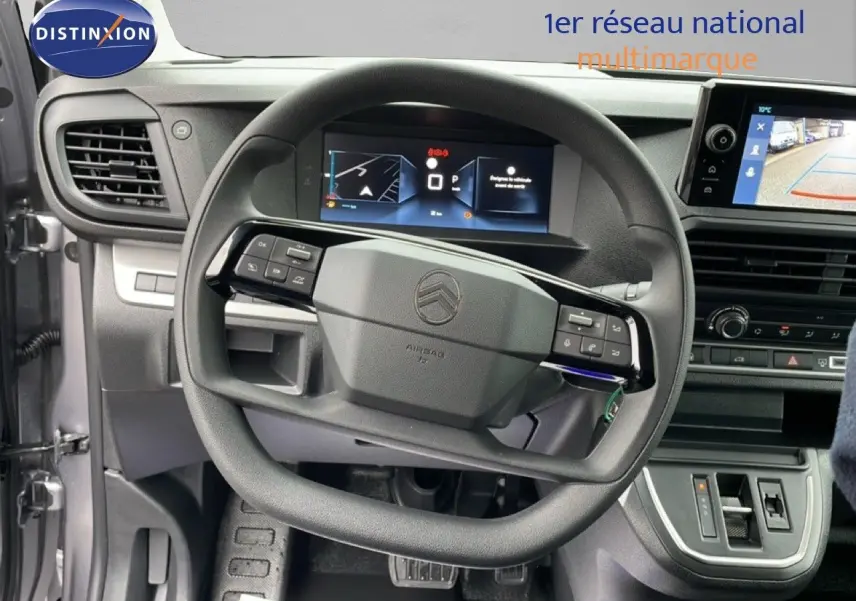 Vue intérieure centrée sur le volant du Citroën Jumpy gris, avec tableau de bord numérique et écran de caméra de recul.