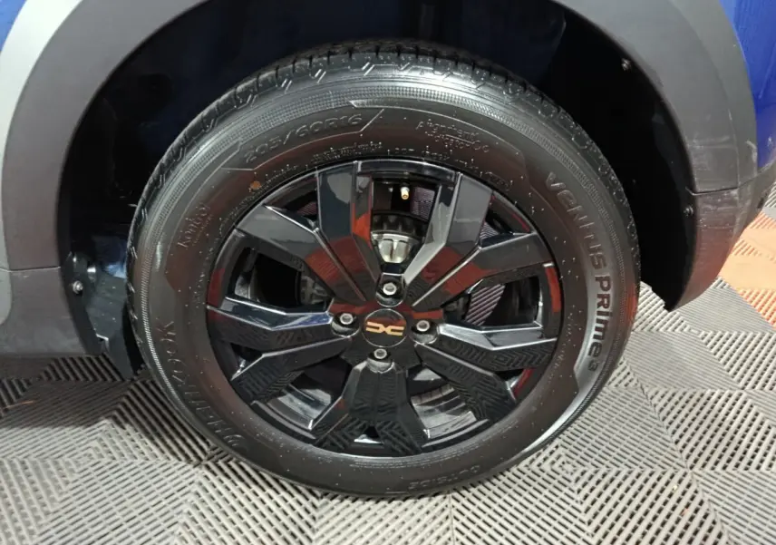 Gros plan sur la roue avant droite noire brillante du Dacia Sandero Extreme+ bleu 2024, avec jante design et logo central.