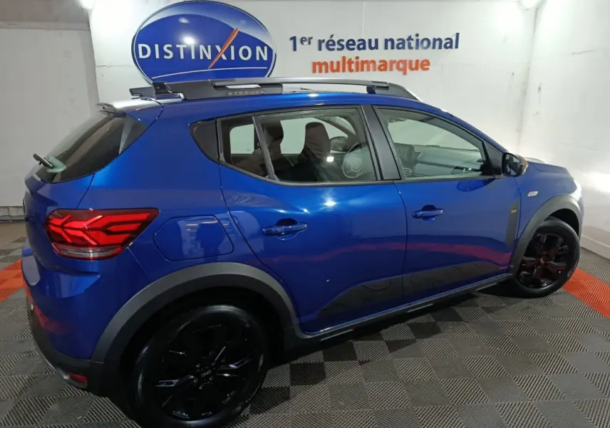 Vue latérale droite d'une Dacia Sandero Extreme+ TCe 110 2024 bleu avec jantes noires et barres de toit assorties.