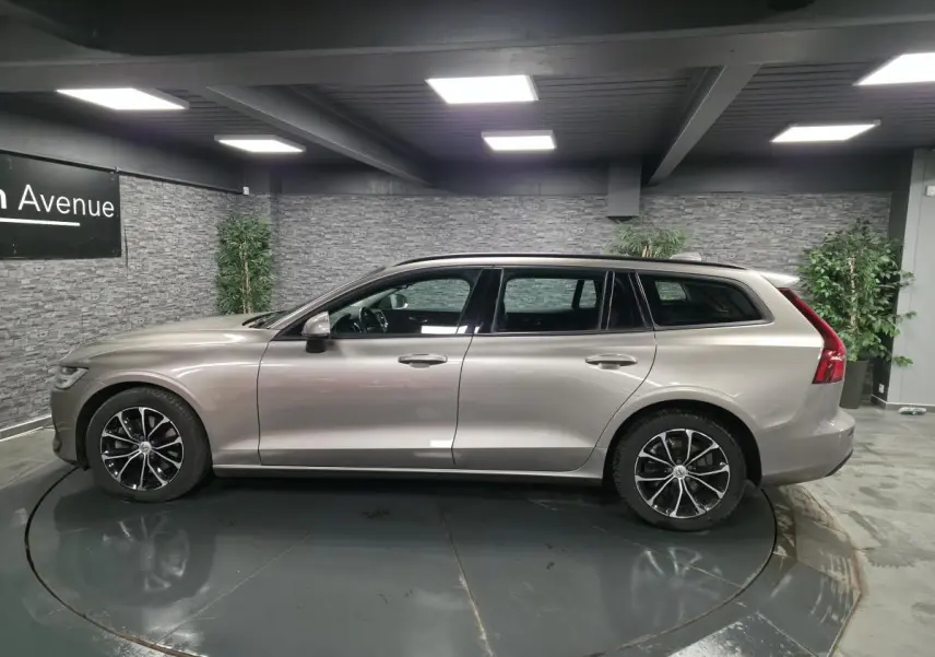 Vue de profil côté gauche d'une Volvo V60 gris métallisé avec jantes alliage 17 pouces en intérieur showroom.