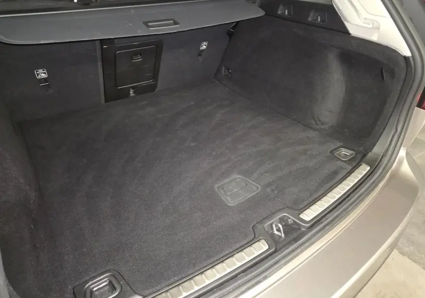 Coffre spacieux gris d'une Volvo V60 B4 Momentum Essentiel 2021, vue intérieure arrière avec tapis noir.
