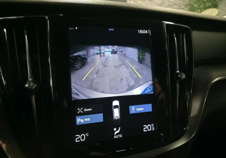 Écran tactile intérieur montrant la caméra de recul d'une Volvo V60 gris, avec lignes de guidage jaunes visibles.