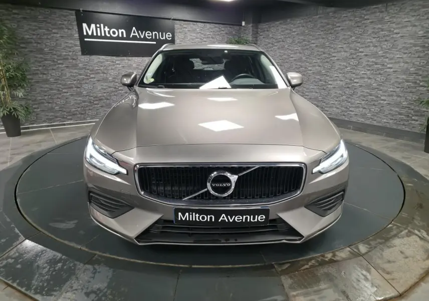 Vue frontale d'une Volvo V60 gris métallisé 2021 avec calandre chromée et phares LED allumés.