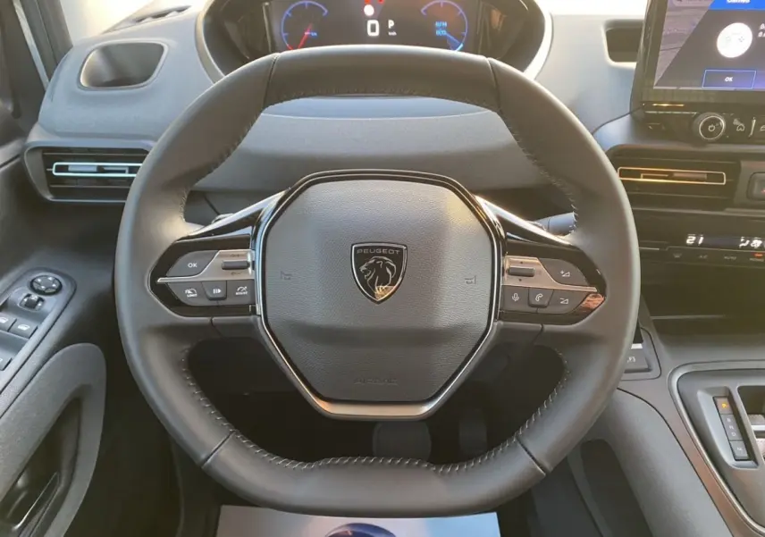 Vue rapprochée du volant cuir noir du Peugeot Rifter III Ph.2 avec commandes intégrées et tableau de bord digital.