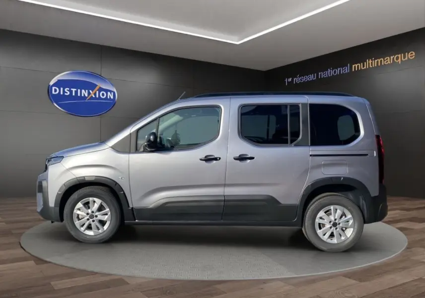 Profil droit d'un Peugeot Rifter gris clair 2026 en présentation showroom avec jantes alliage et protections noires.