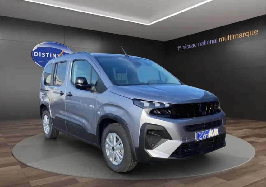 Peugeot Rifter gris clair en 3/4 avant droit, avec calandre noire et jantes argentées, en intérieur showroom.