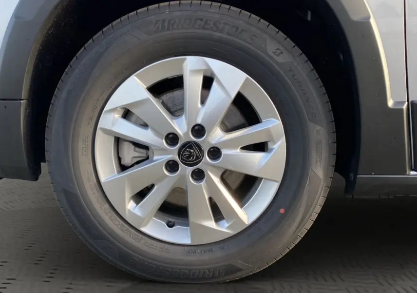 Gros plan sur la roue avant droite du Peugeot Rifter gris clair, jante alliage à 5 doubles branches et logo lion central.