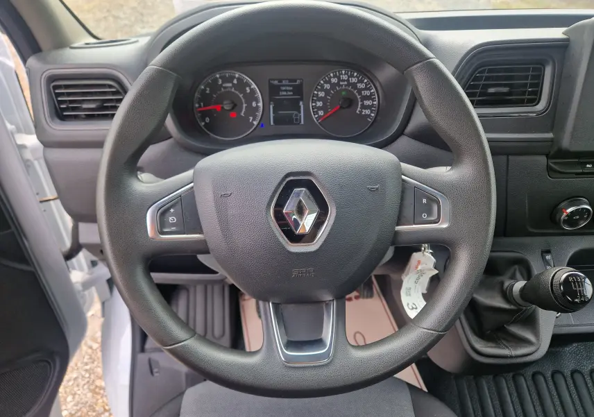 Vue intérieure centrée sur le volant noir Renault d’un Master Châssis Cabine blanc avec tableau de bord et levier de vitesse manuel.