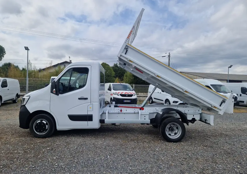 Vue de profil côté gauche d’un Renault Master blanc avec benne basculante levée et roues jumelées arrière.