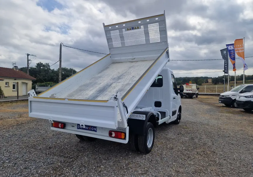 Renault Master Châssis cabine blanc vu 3/4 arrière avec benne relevée et roues jumelées sur terrain extérieur.