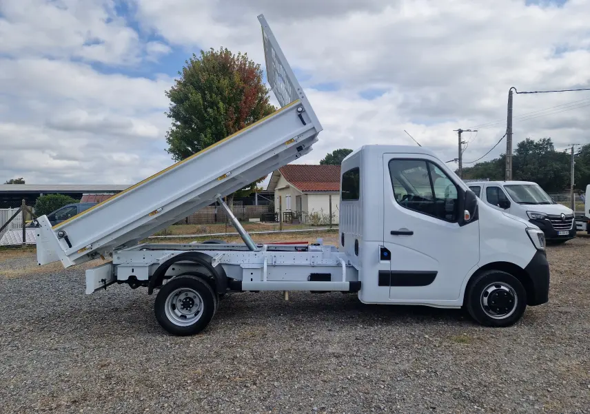 Vue de profil droit d’un Renault Master blanc 2024 avec benne basculante relevée et roues jumelées arrière.