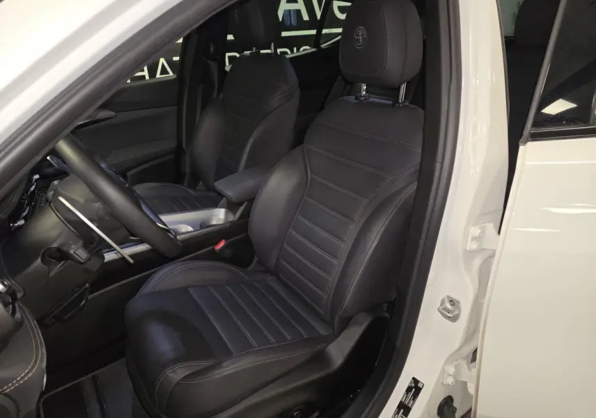 Vue intérieure côté conducteur de l'Alfa Romeo Tonale blanc, mettant en valeur les sièges sport en cuir noir et le volant.