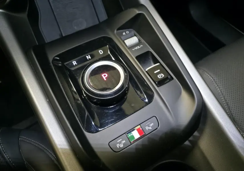 Gros plan sur la molette de boîte automatique et commandes de stationnement de l'Alfa Romeo Tonale blanche, intérieur noir.