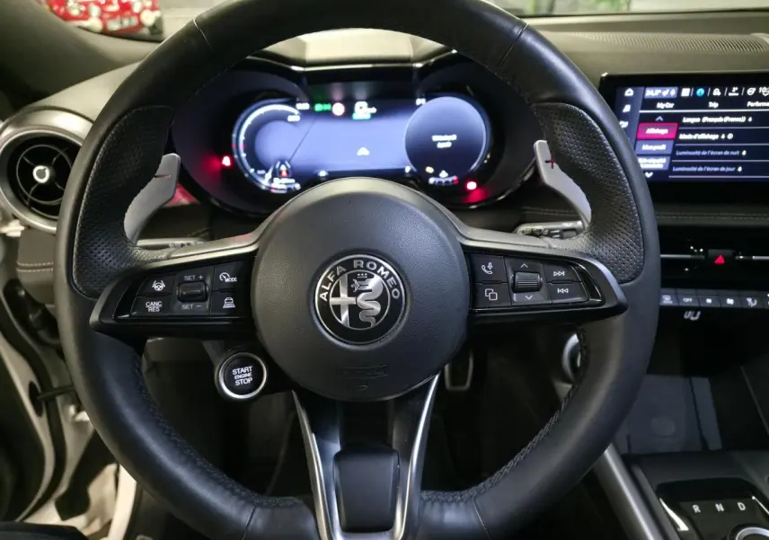 Vue rapprochée du volant en cuir noir perforé de l'Alfa Romeo Tonale 2025 avec tableau de bord digital et écran tactile.