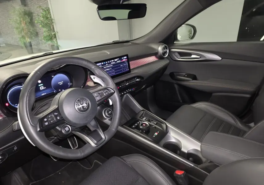 Vue intérieure côté conducteur de l'Alfa Romeo Tonale 2025, volant cuir noir et tableau de bord digital avec inserts rouges.