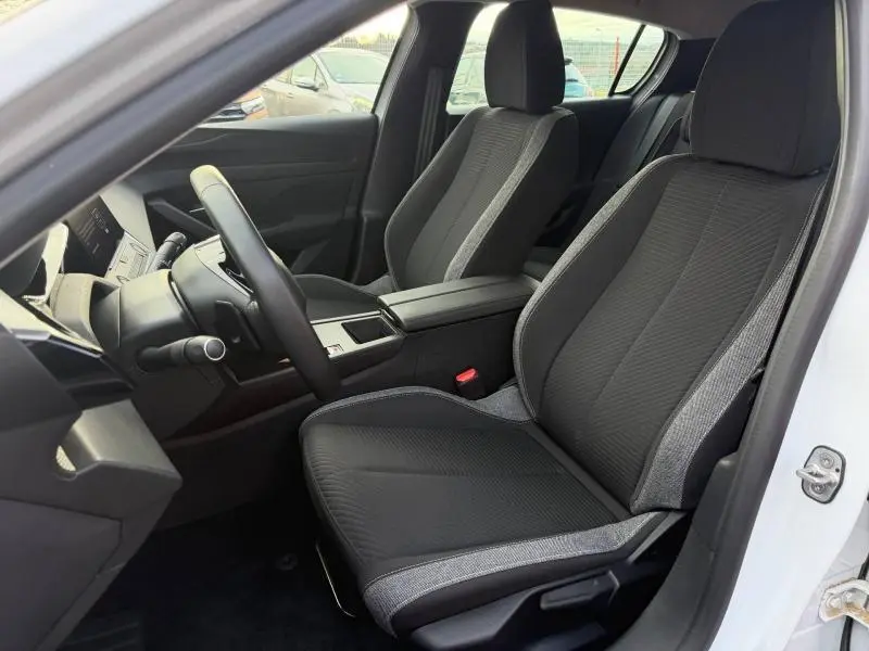 Vue intérieure côté conducteur de la Peugeot 308 2024 blanc Okénite, sièges tissu noir avec surpiqûres grises.