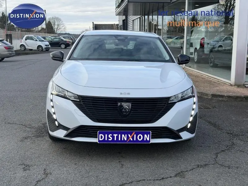 Vue avant frontale d'une Peugeot 308 blanche Okénite 2024 avec calandre noire et feux LED verticaux allumés.