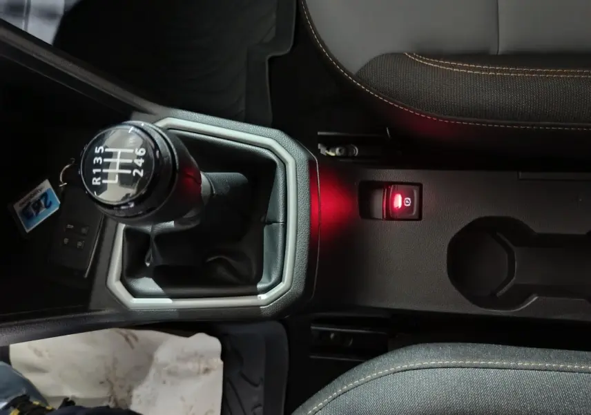 Vue rapprochée de la console centrale noire avec levier de vitesse manuel et frein à main électrique rouge d’une Dacia Sandero bleu 2024.