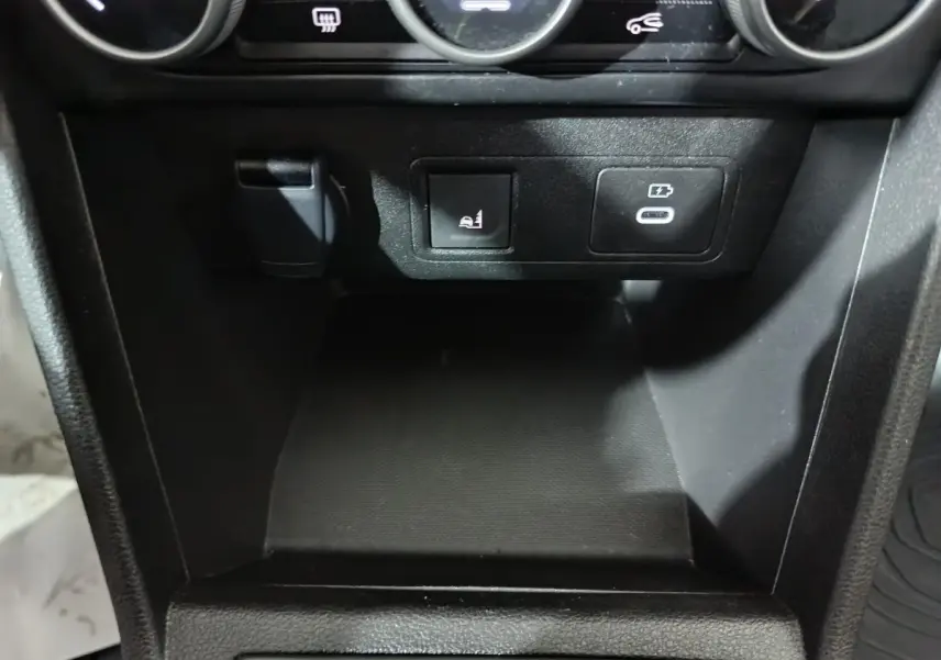 Gros plan sur la console centrale noire de la Dacia Sandero 2024, montrant prises 12V et USB avec bouton de siège chauffant.