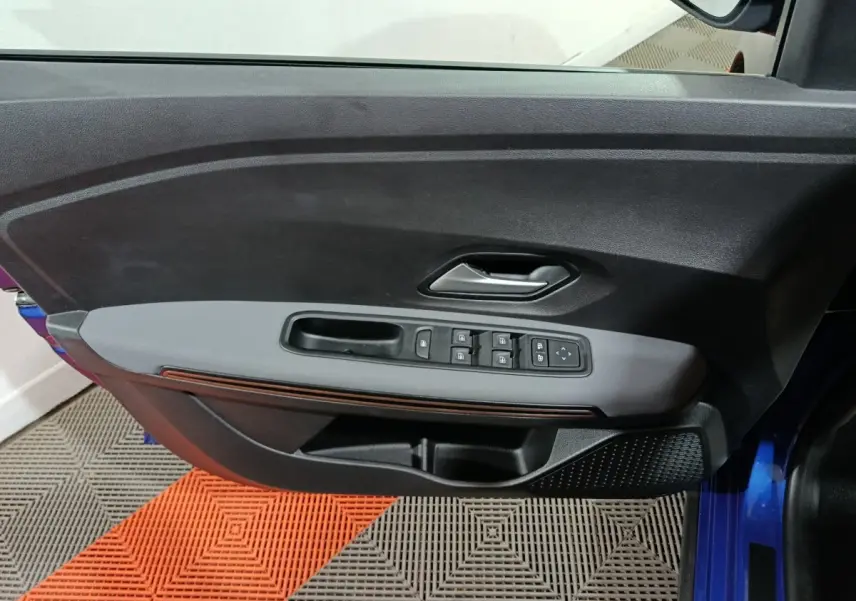 Vue rapprochée de la porte avant gauche bleu de la Dacia Sandero Extreme+ avec commandes électriques et poignée intégrée.