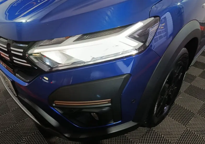Gros plan sur l'avant droit bleu d'une Dacia Sandero Extreme+ 2024, mettant en valeur le phare LED et la calandre noire.