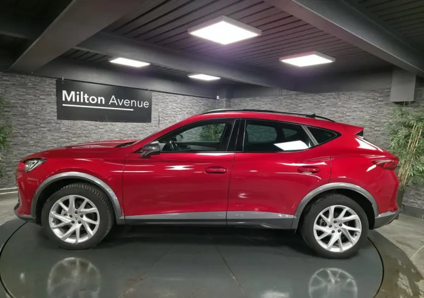 Vue latérale droite d'un CUPRA Formentor rouge avec jantes alliage 18'', entourages d'ailes gris et toit noir en intérieur showroom.
