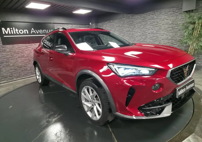 Vue 3/4 avant droite d'une CUPRA Formentor rouge Désir avec projecteurs LED et jantes alliage 18 pouces dans un showroom.