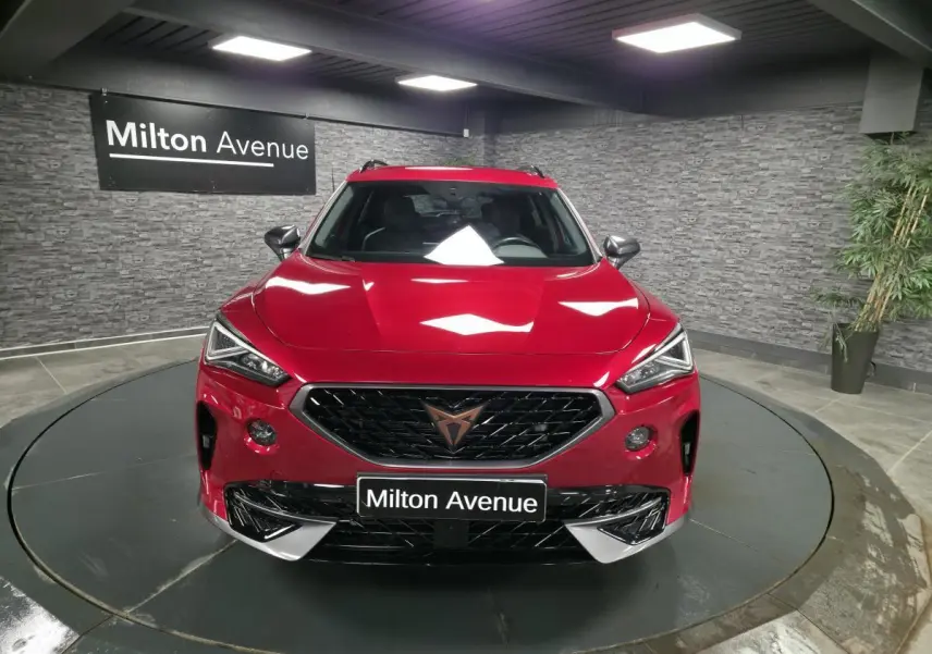 Vue avant d'un CUPRA Formentor rouge avec calandre noire et logo cuivre, dans un showroom au sol circulaire.
