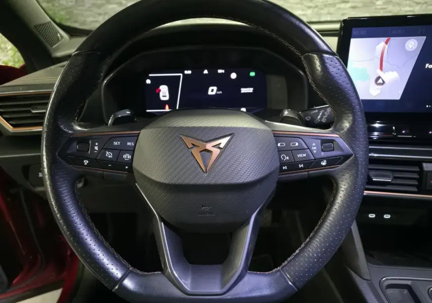 Vue rapprochée du volant cuir perforé noir avec logo CUPRA cuivre et tableau de bord digital du Formentor rouge.