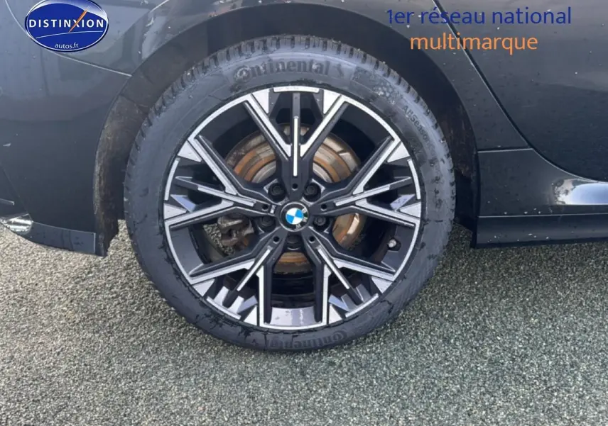 Gros plan sur la roue arrière droite noire d'une BMW Série 1 120da 2024 avec jante alu design sportif.