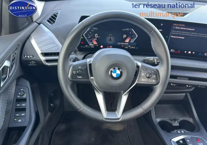 Vue intérieure centrée sur le volant noir multifonction d'une BMW Série 1 120da 2024 avec tableau de bord digital.