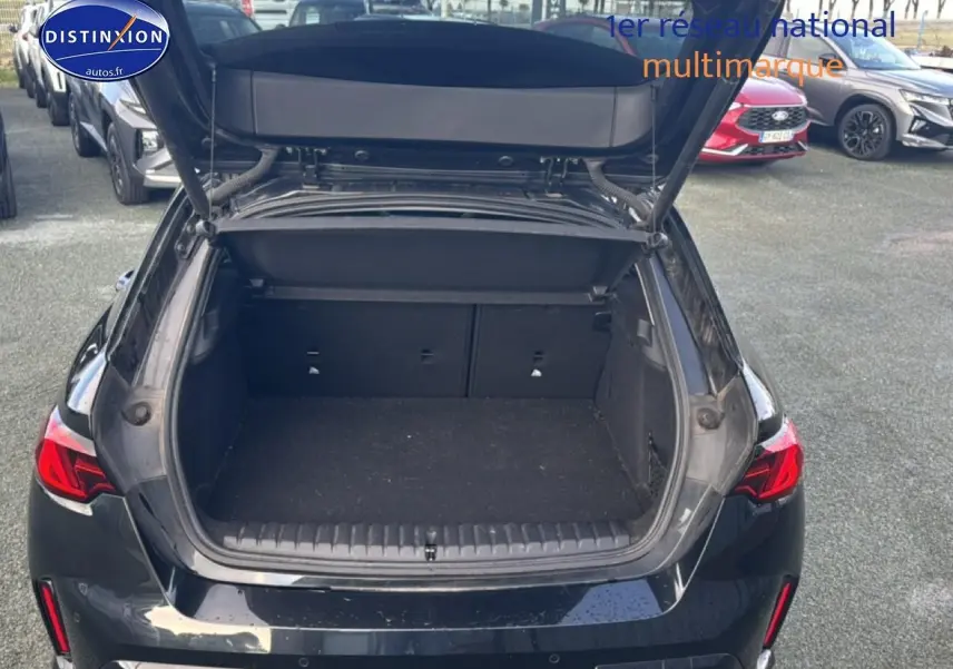 Vue arrière d'une BMW Série 1 noire 2024 avec coffre ouvert, montrant l'espace de chargement vide.