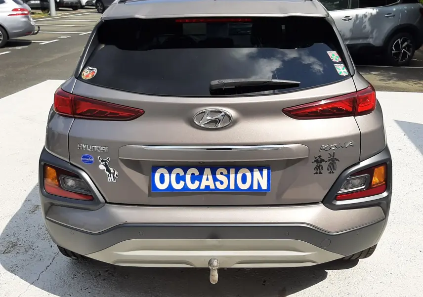 Vue arrière d'un Hyundai Kona gris 2018 avec stickers décoratifs et plaque "OCCASION" visible sur un parking.