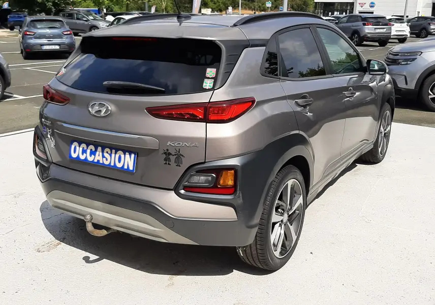 Vue 3/4 arrière droite d'un Hyundai Kona gris 2018 avec stickers décoratifs sur le hayon, stationné en extérieur.