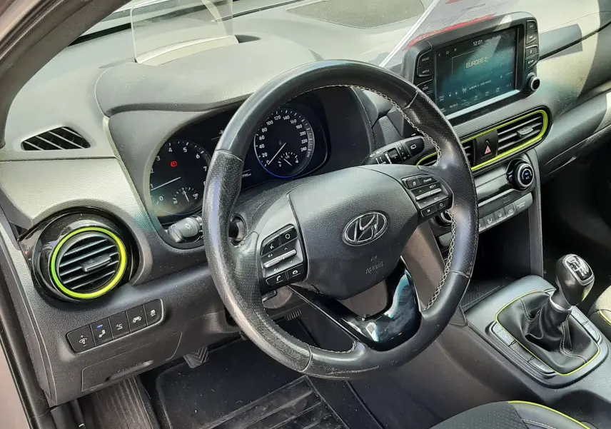 Vue intérieure côté conducteur du Hyundai Kona gris 2018, volant cuir, tableau de bord avec écran tactile et levier de vitesse manuel.