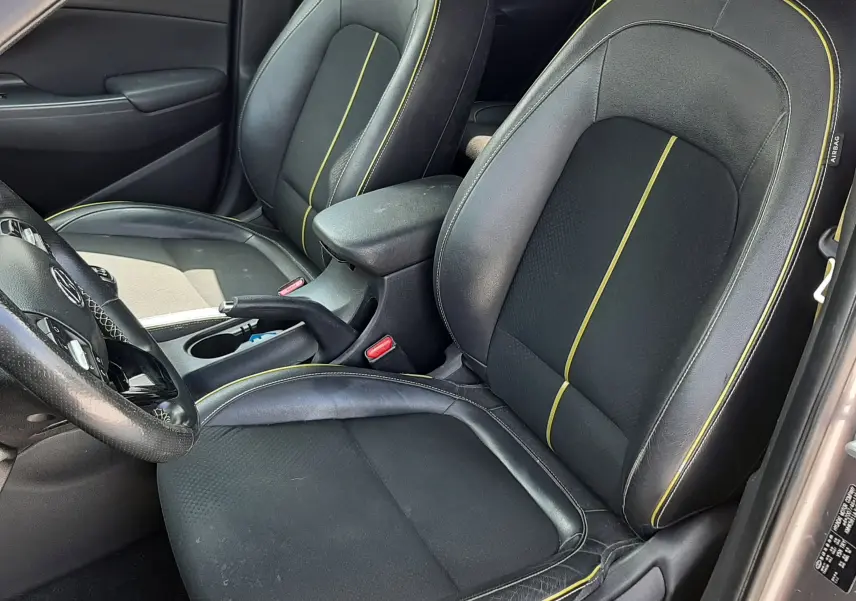 Vue intérieure côté conducteur du Hyundai Kona 2018, sièges noirs avec surpiqûres jaunes et volant partiellement visible.