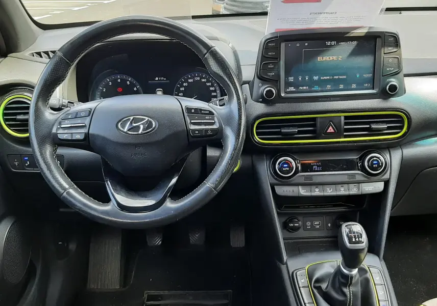Vue intérieure avant du Hyundai Kona gris 2018, volant multifonction, écran tactile, et levier de vitesse manuel avec surpiqûres jaunes.
