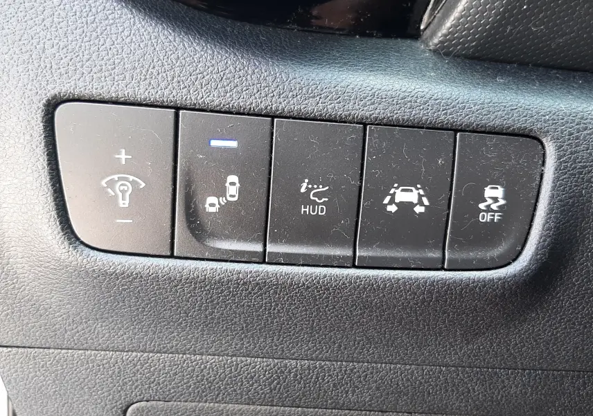 Gros plan sur les boutons de commande du tableau de bord du Hyundai Kona gris 2018, avec témoin lumineux bleu allumé.