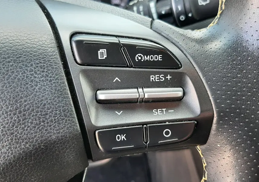 Gros plan sur les commandes au volant côté droit du Hyundai Kona gris, avec boutons de régulateur de vitesse et mode.