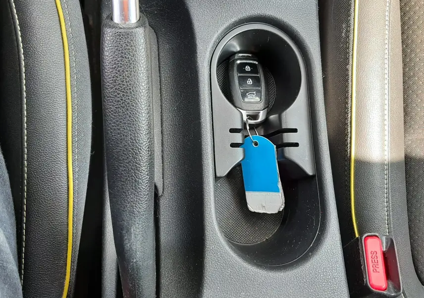 Vue rapprochée de la console centrale noire avec frein à main, porte-clés Hyundai et surpiqûres jaunes des sièges gris.