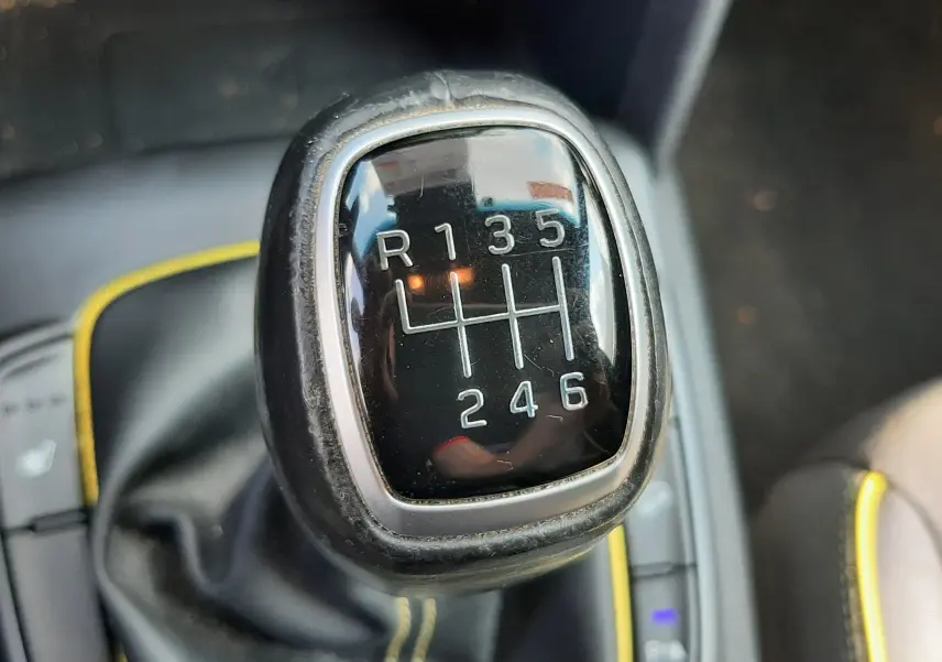 Gros plan sur le levier de vitesses manuel noir avec surpiqûres jaunes dans l'habitacle d'une Hyundai Kona gris 2018.