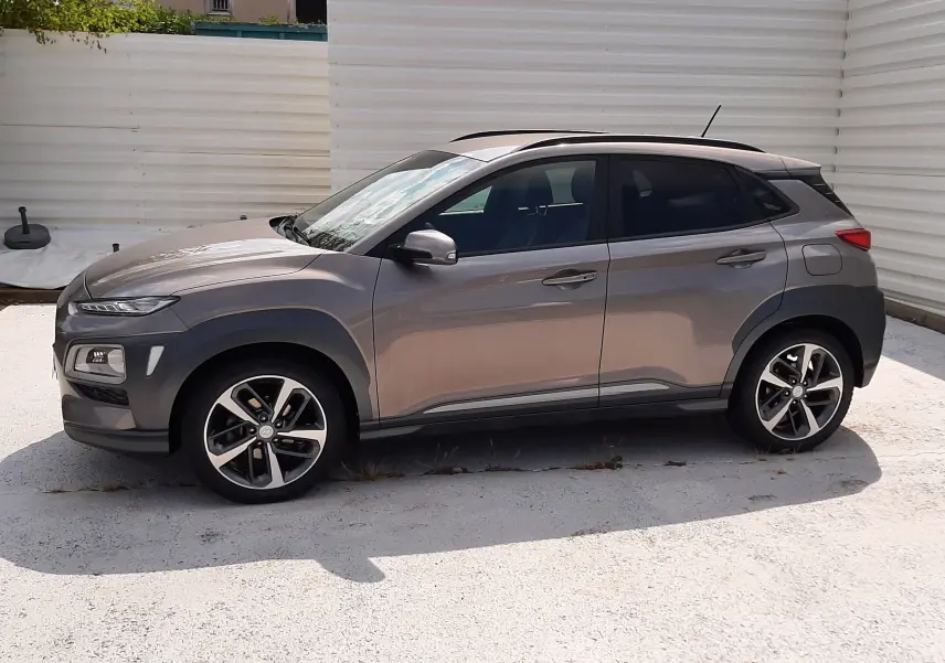 Vue de profil côté gauche d'un Hyundai Kona gris 2018 avec toit noir et jantes alliage bicolores.