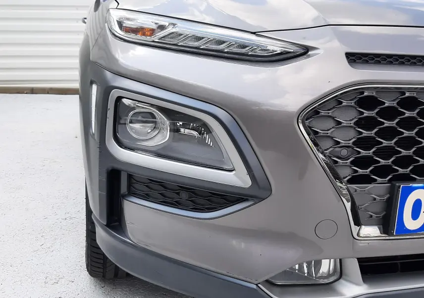 Vue rapprochée 3/4 avant gauche du Hyundai Kona gris, mettant en valeur ses phares et la calandre hexagonale.