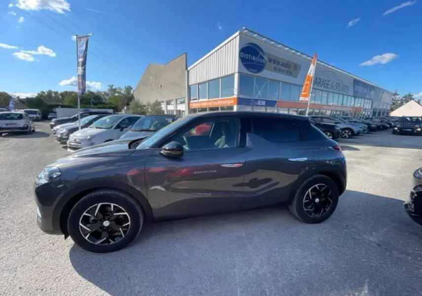 Vue de profil côté gauche d’un DS3 Crossback E-Tense gris platinium avec jantes noires et toit noir, stationné en extérieur.