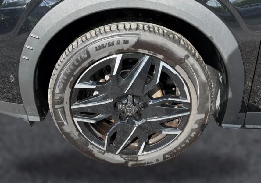 Gros plan sur la roue avant gauche noire d’un Peugeot 3008 1.2 hybrid 145 allure e-dcs6 avec jante alu bicolore.