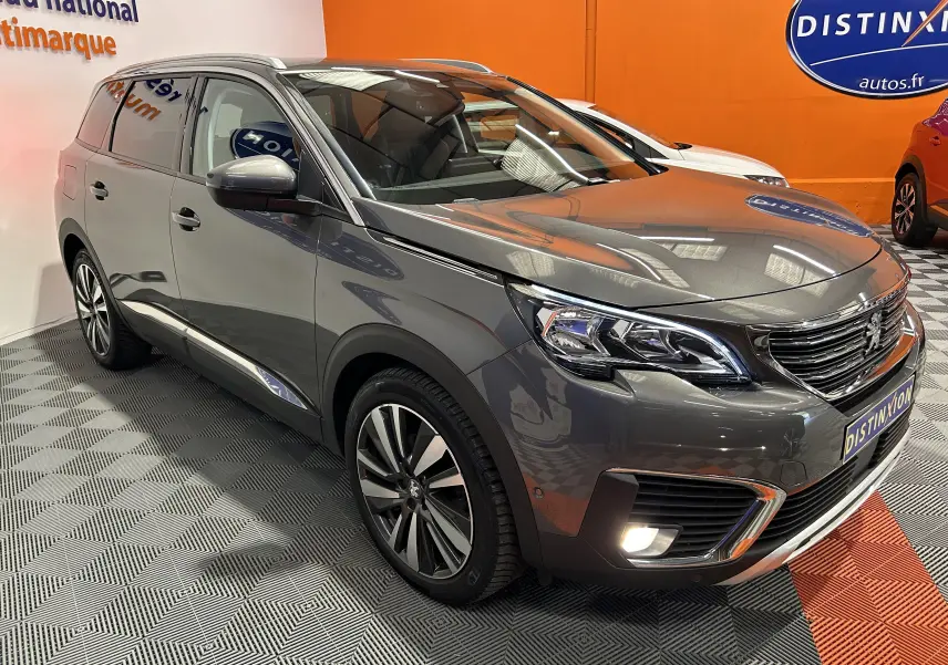 Peugeot 5008 gris métallisé vue 3/4 avant droit en intérieur, avec phares LED et jantes alliage distinctives.